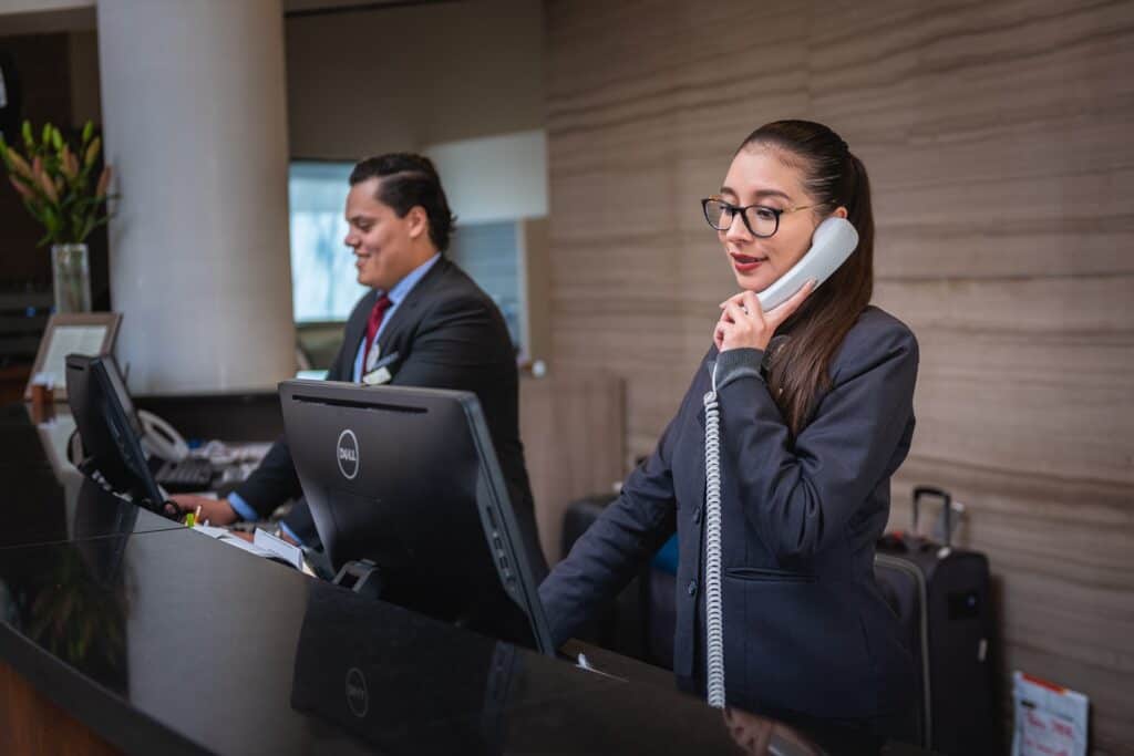 A staff member at the hotel front desk communicates verbally with a guest on the phone.