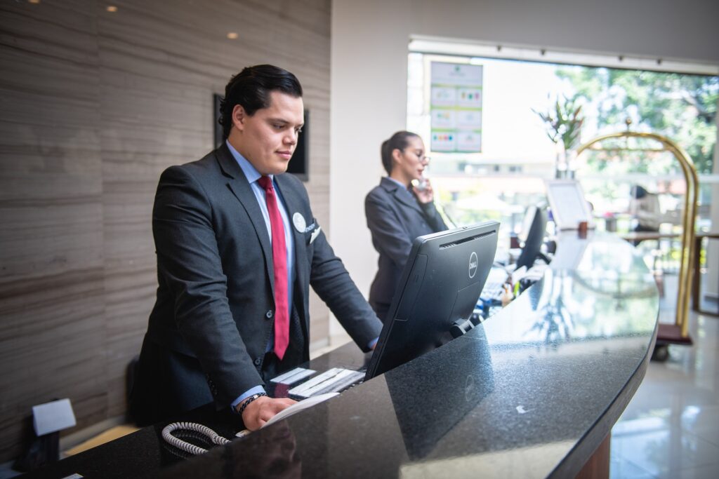 A staff member at the hotel front desk communicates verbally with a guest on the phone.