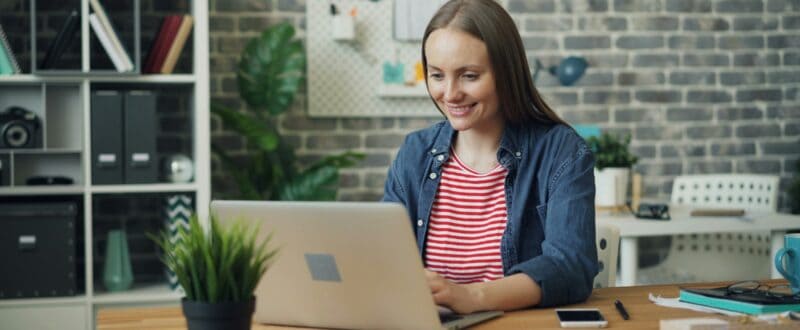 A guest planning a trip sits with her laptop and mobile phone at her desk.