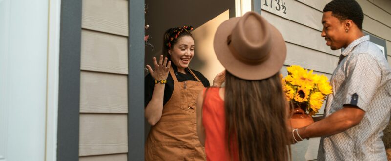 A host greets two guests at the door of their vacation rental property.