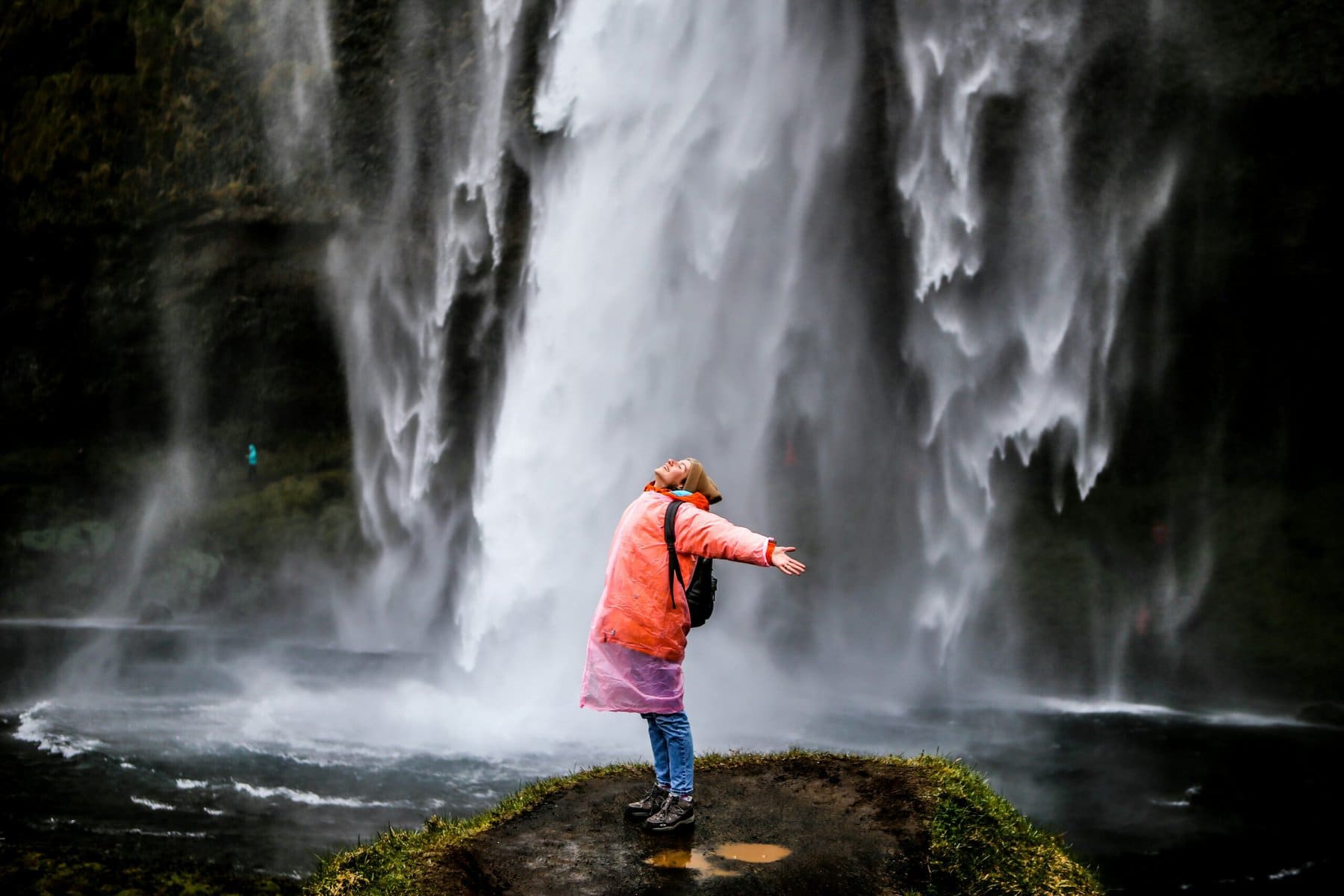 A traveler stands under a waterfall with arms outstretched, enjoying the unique guest experience offered as an extra with their accommodation booking.